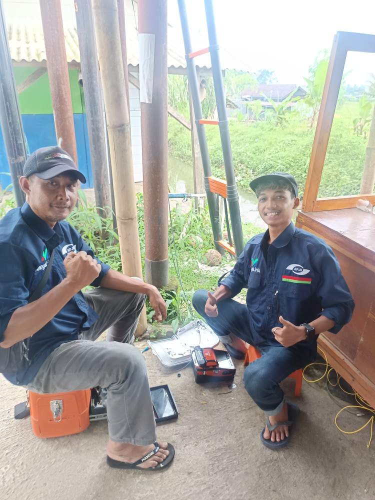 Dua teknisi Megalink berseragam melakukan splicing fiber optik dengan fusion splicer di lapangan