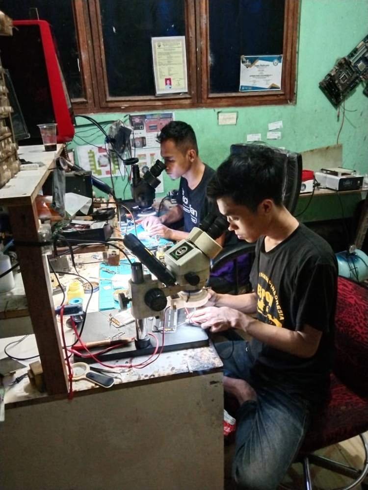 Teknisi memperbaiki motherboard HP menggunakan mikroskop di bengkel